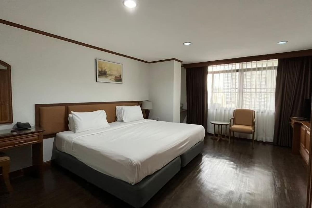 A hotel room with a large bed, a desk, a chair, and a window with curtains.