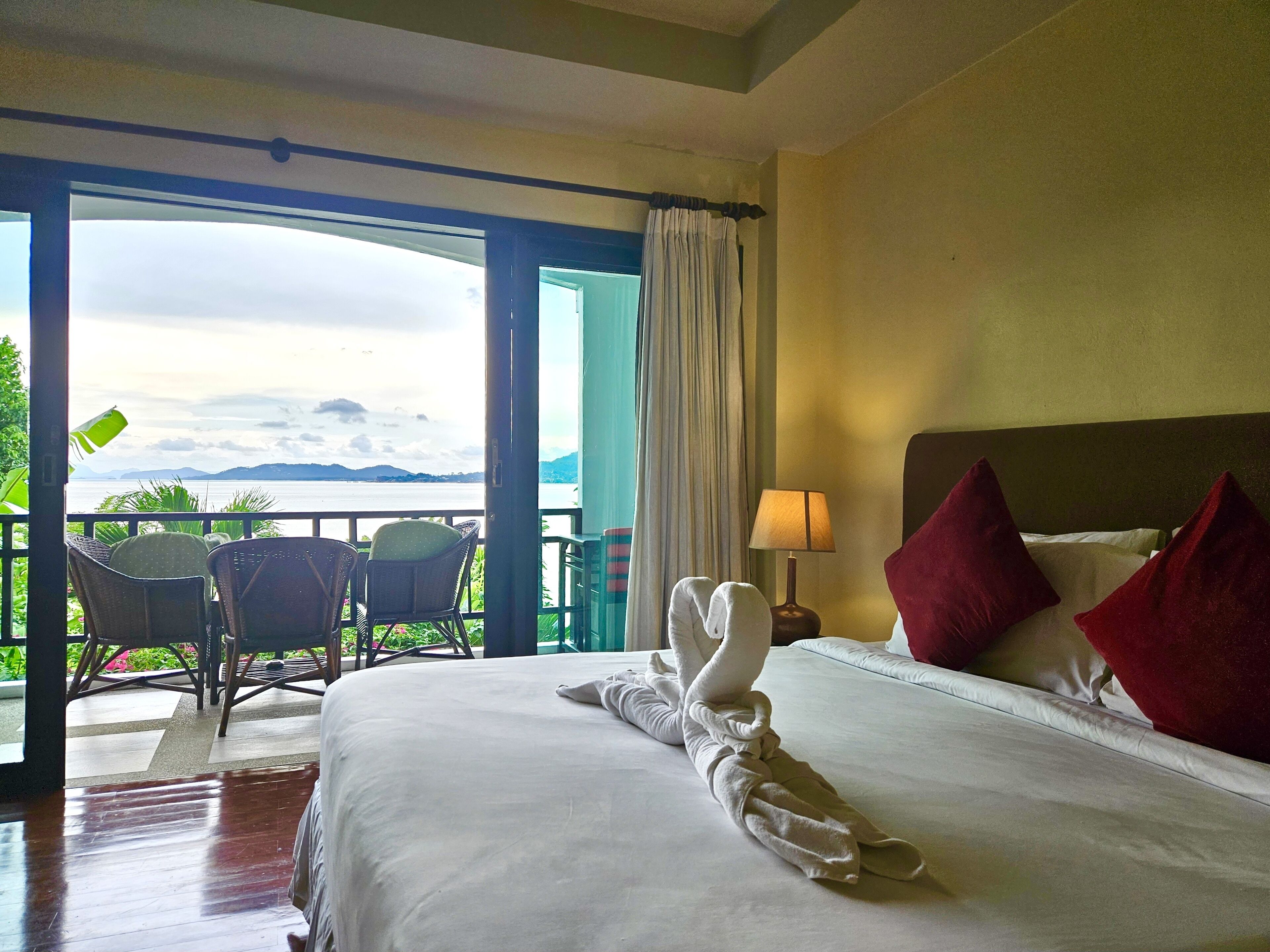 A hotel room with a bed, a nightstand, a lamp, a chair, and a view of the sea.