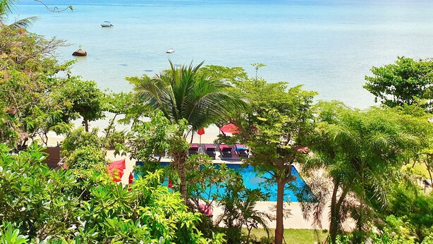 A view of a pool surrounded by lush greenery, overlooking a calm sea with boats and distant mountains. - Cinnamon Beach Villas (Koh Samui)