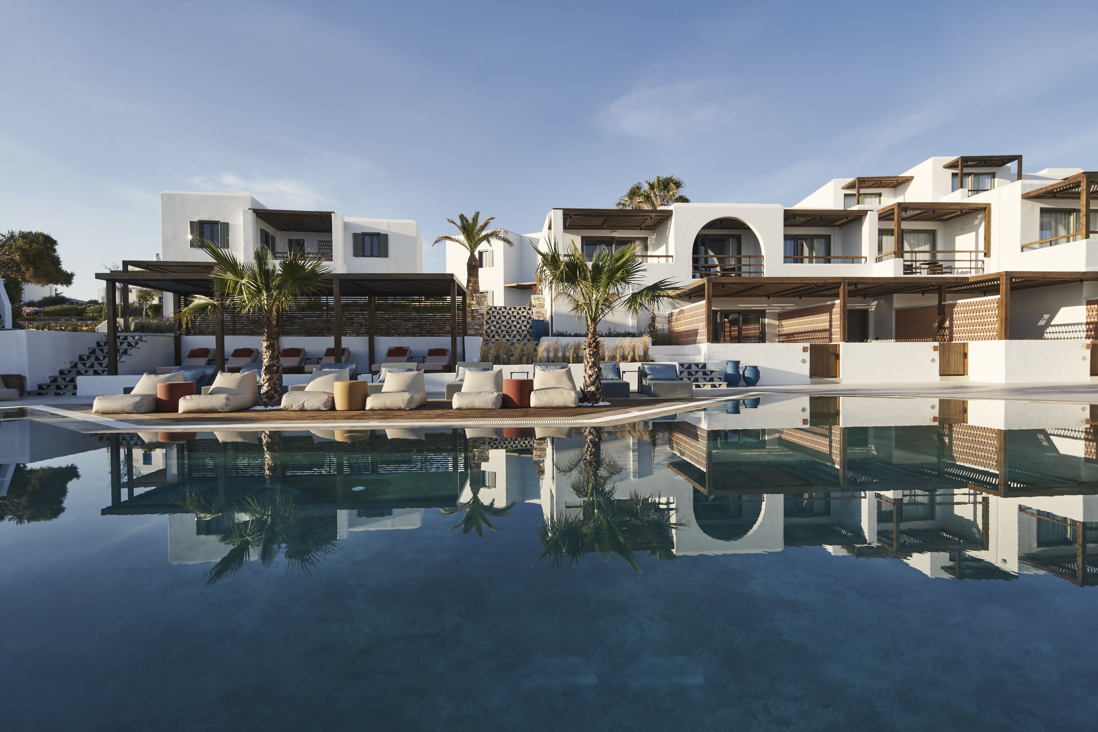 A modern resort with a clear swimming pool, lounge area with sun loungers, and a multi-story building with balconies.