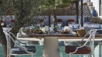 A poolside area with two white metal chairs, a table with a drink, and a pool in the background.