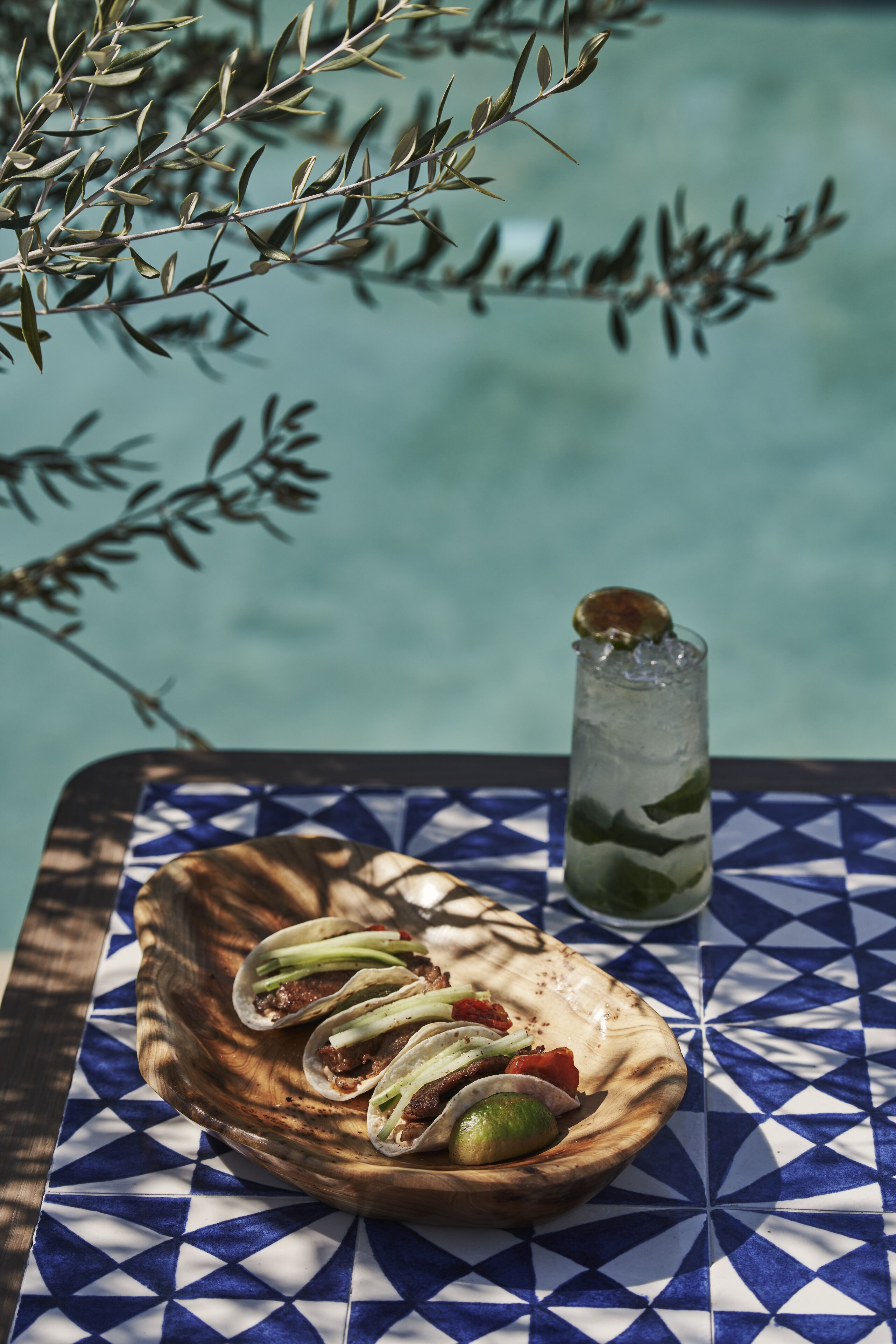A wooden bowl with tacos and a lime on a table with a blue and white geometric pattern.