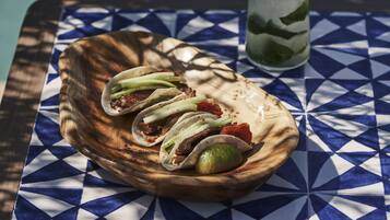 A wooden bowl with tacos and a lime on a table with a blue and white geometric pattern.