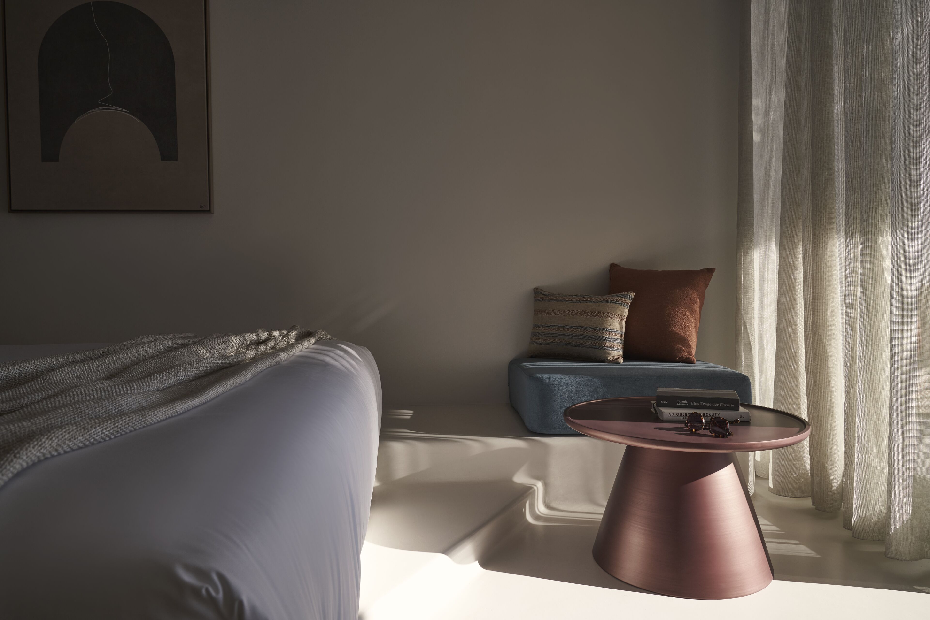 A modern bedroom with a bed, a blue sofa, a pink side table, and a window with sheer curtains.