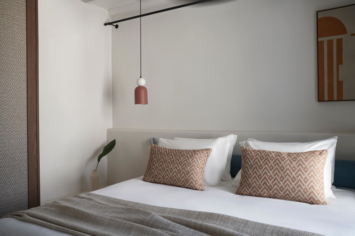 Una cama bien hecha con almohadones estampados, una lámpara colgante y un diseño de pared minimalista.