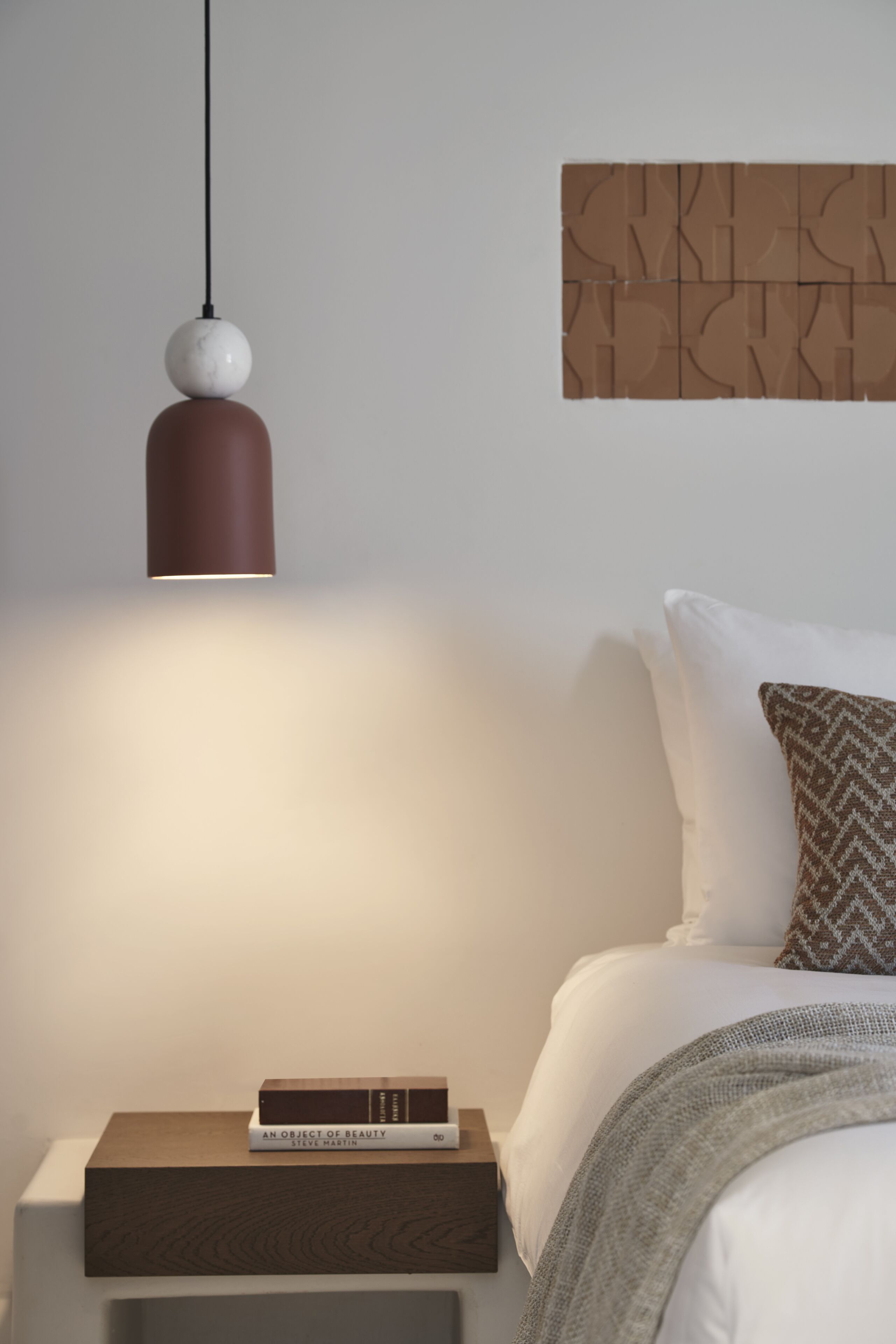 Une chambre à coucher avec un lit, une table de chevet sur laquelle se trouve un livre, une horloge murale et une lampe suspendue.