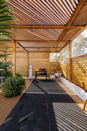 Un espace extérieur abrité, doté d’un toit en lattes de bois, d’un tapis noir et d’un banc.