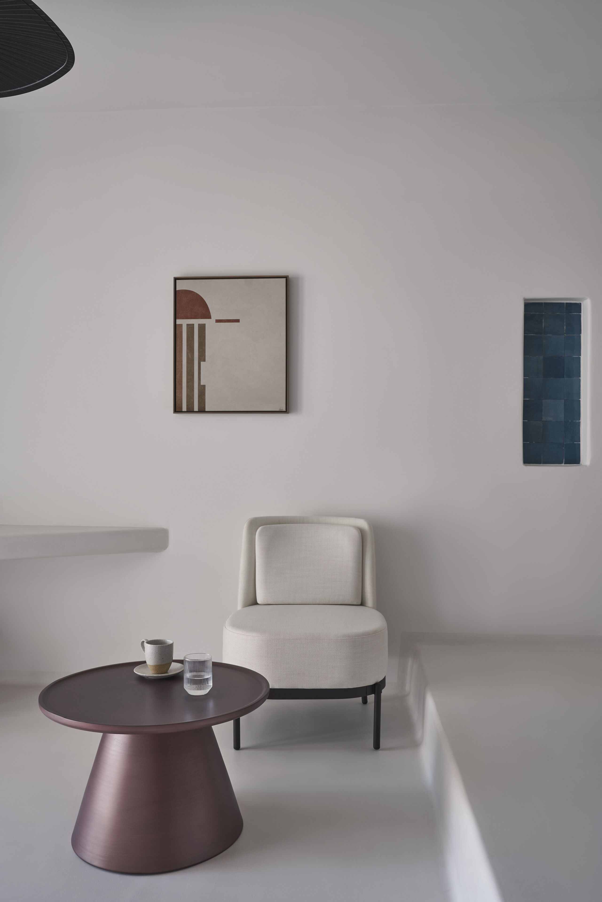 Una habitación minimalista con una mesa redonda, una silla y un cuadro abstracto colgado en la pared.