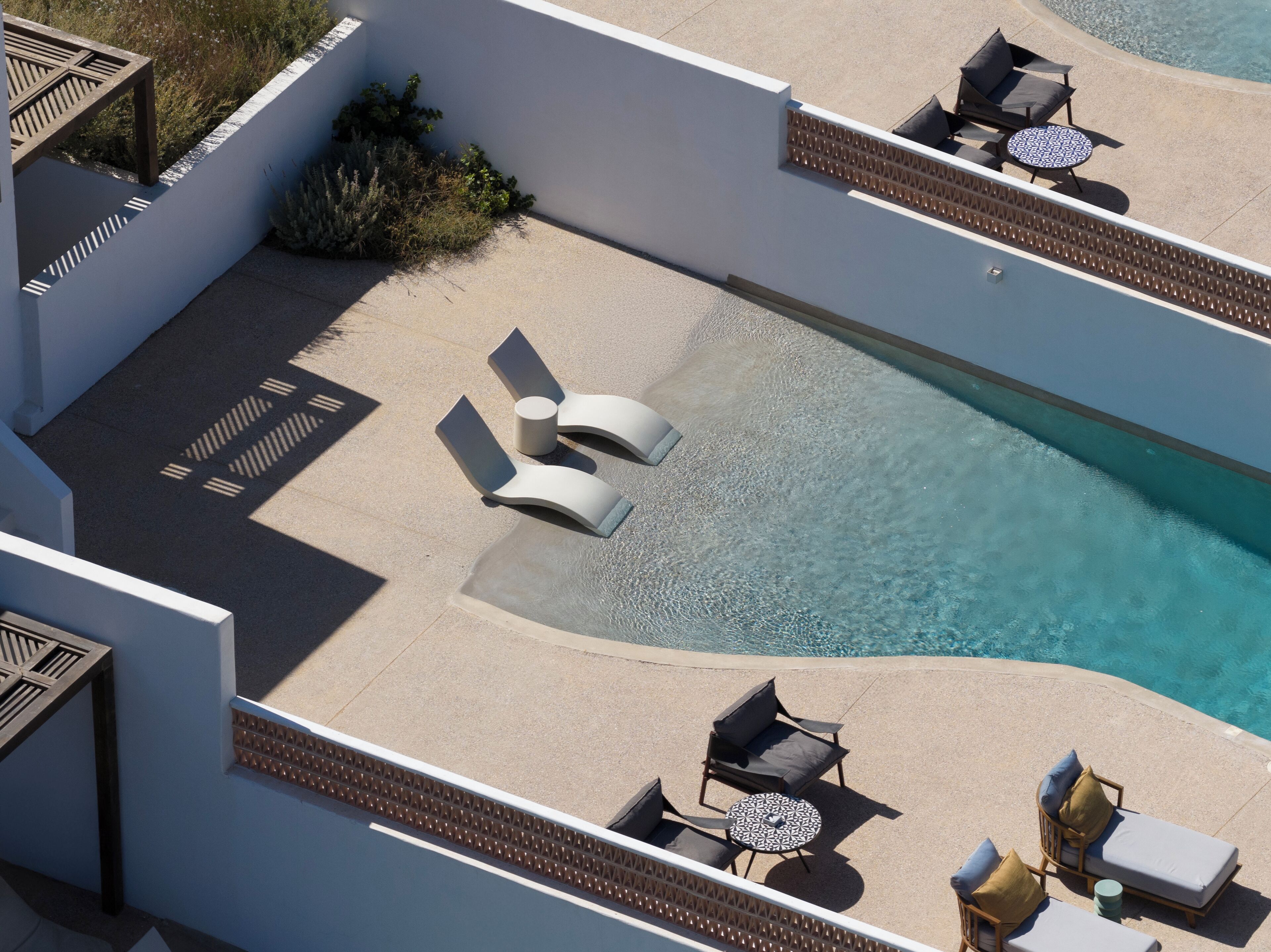 Vue aérienne d’un espace piscine sur le toit, avec des chaises longues, une petite table et une piscine à l’eau d’un bleu limpide.