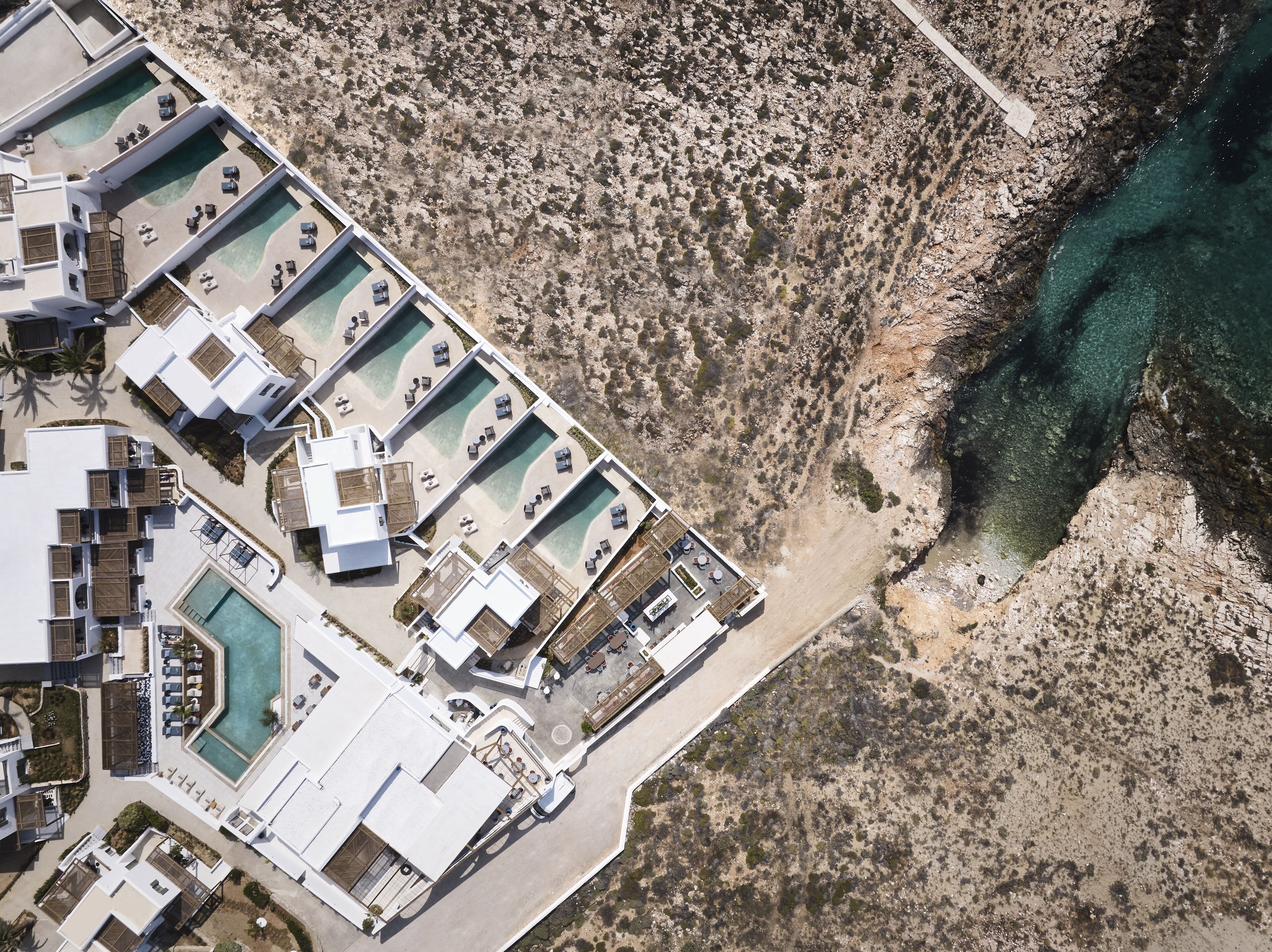 An aerial view of a resort with multiple swimming pools, a rocky coastline, and a clear view of the sea.