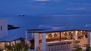 A modern outdoor bar area with a view of the sea, featuring a bar counter, seating, and ambient lighting.