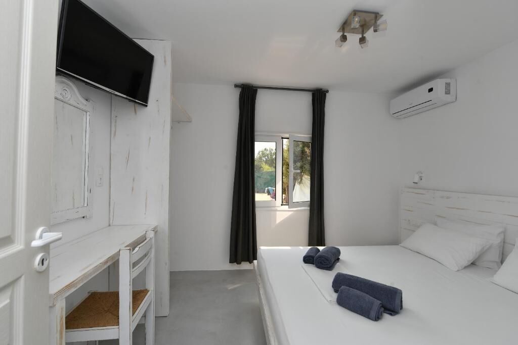 Une chambre à coucher avec un lit, un téléviseur fixé au mur, une fenêtre avec des rideaux et un appareil de climatisation.