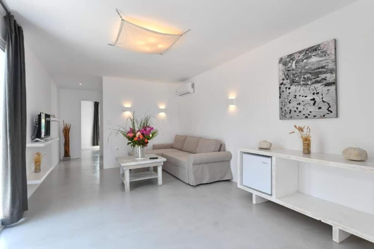 Ein modernes Wohnzimmer mit einer Couch, einem Couchtisch mit Blumen, einem Fernseher und einem Bild an der Wand.