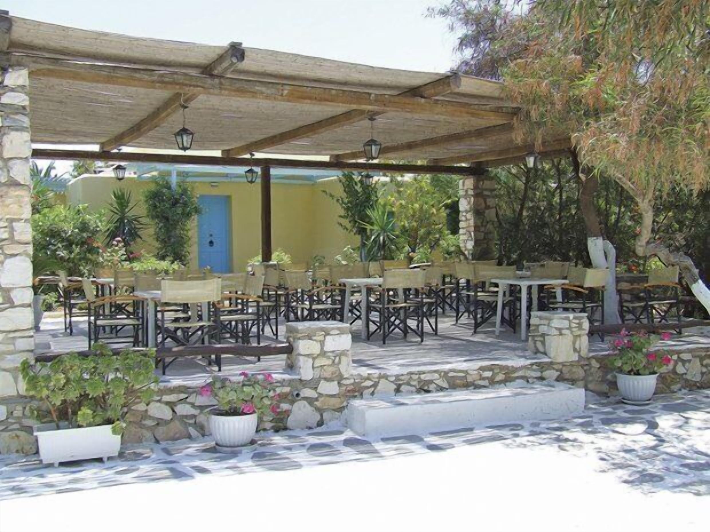 Un patio al aire libre con paredes de piedra, mesas y sillas de madera y plantas en macetas.