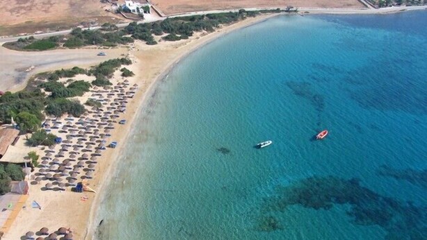 An aerial view of a beach with clear blue water, a sandy shore, and several umbrellas.