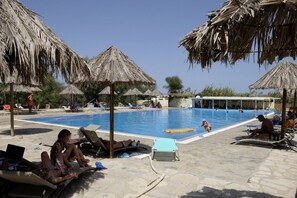 Zona de piscina con sillas de descanso y sombrillas de paja.