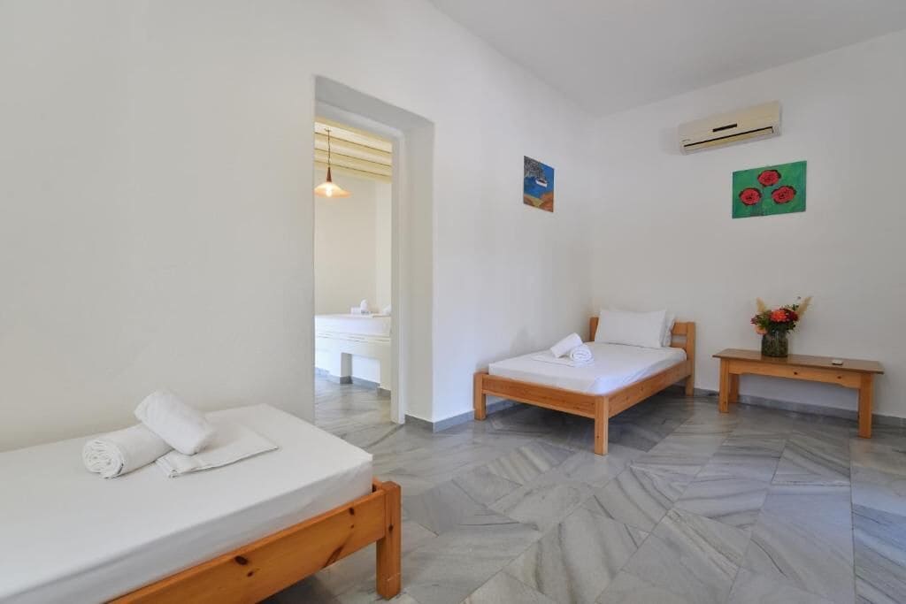 A bedroom with two beds, a wooden nightstand, and a bathroom visible through an open door.