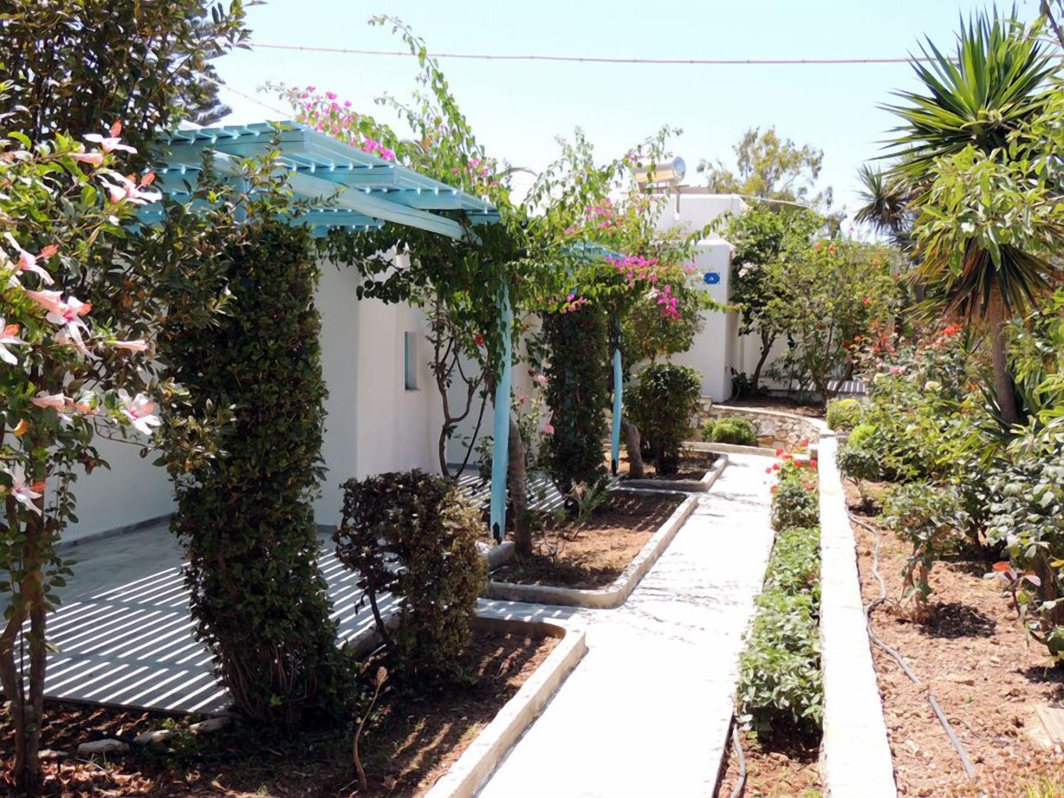 A garden pathway with a pergola covered in climbing plants and flowers, leading to a white building with a blue roof.