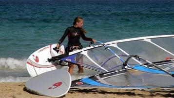 Una persona porta una taula de windsurf i una vela a la platja.