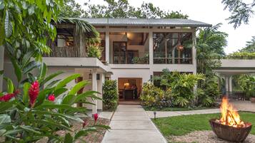 A two-story house with a covered porch, a fire pit, and lush greenery.
