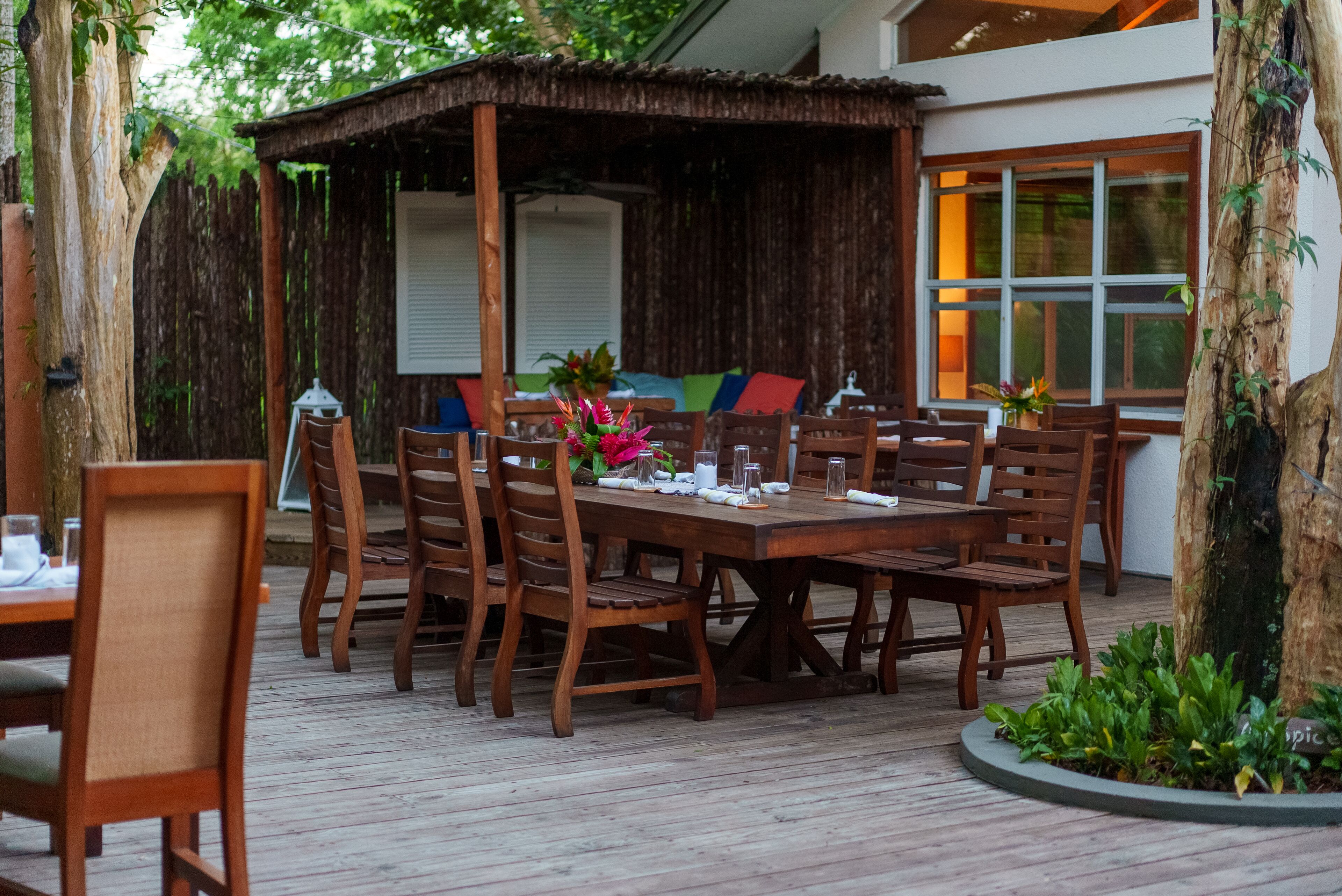 A wooden deck with a dining table and chairs, surrounded by a wooden fence and trees.