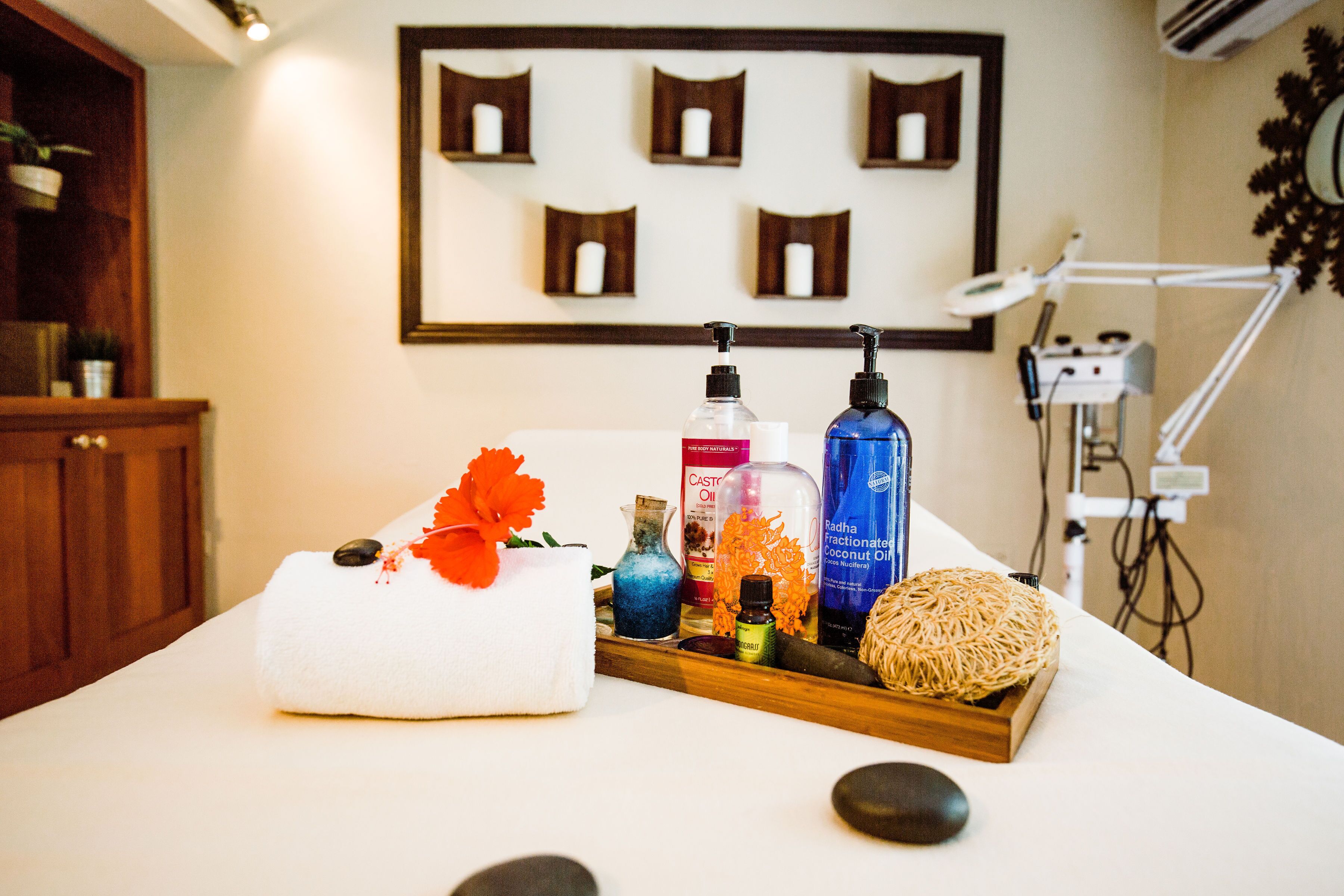 A spa treatment area with a massage table, a tray with various oils and a towel, and a wall-mounted shelf with candles.