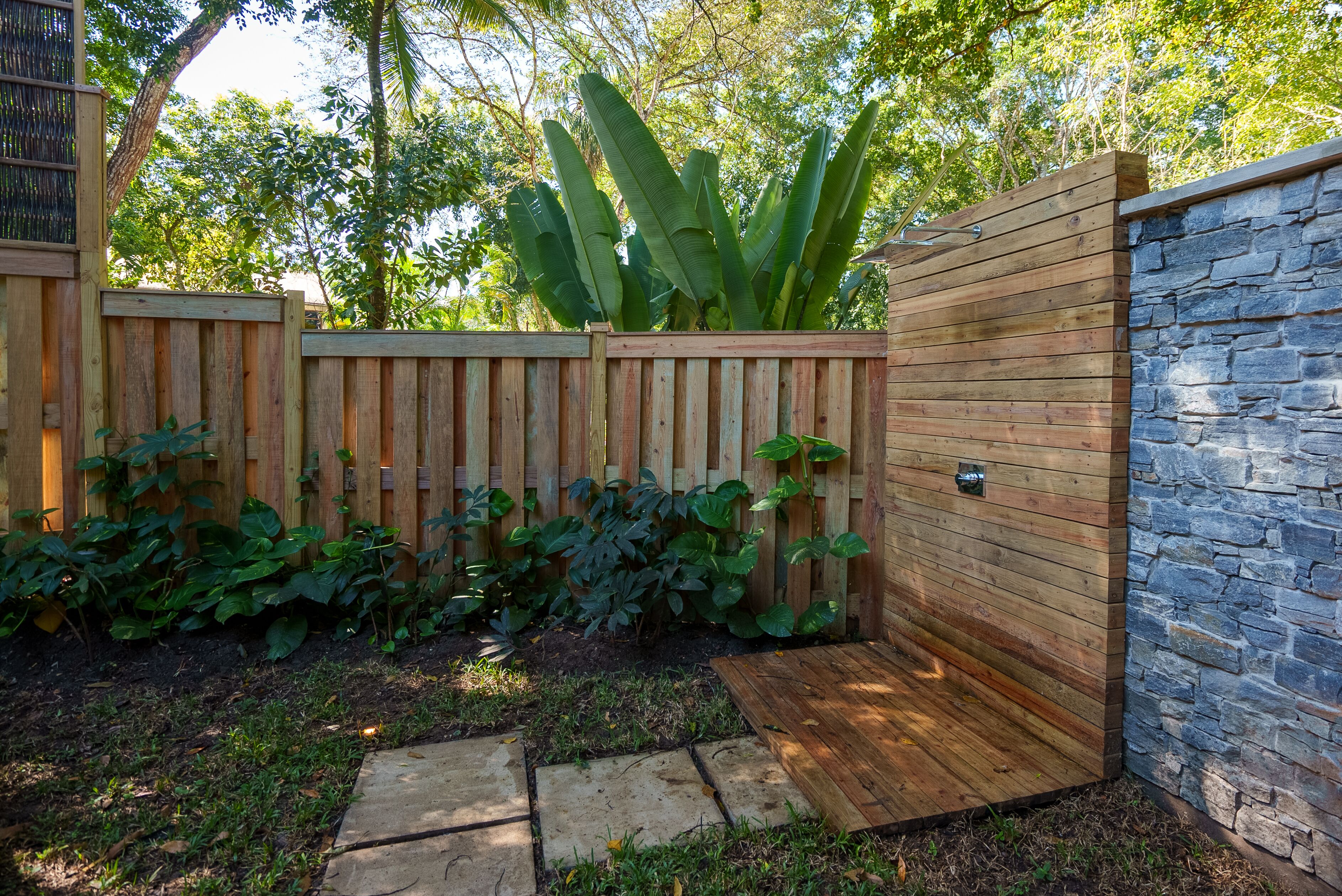 Un recinto in legno con un muro in pietra, immerso nel verde e con un vialetto in cemento.