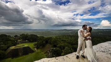 A couple embracing on a high vantage point overlooking a lush landscape with ancient ruins.