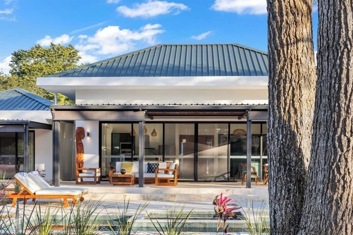 Una casa moderna con un porche techado, ventanas amplias y una piscina.