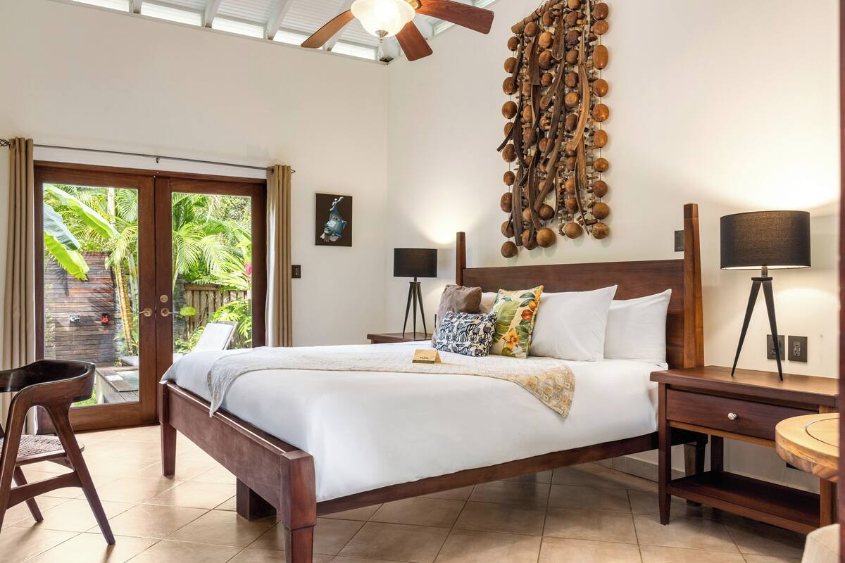 Un dormitorio con cama, mesitas de noche, una silla, ventilador de techo y vistas al exterior.