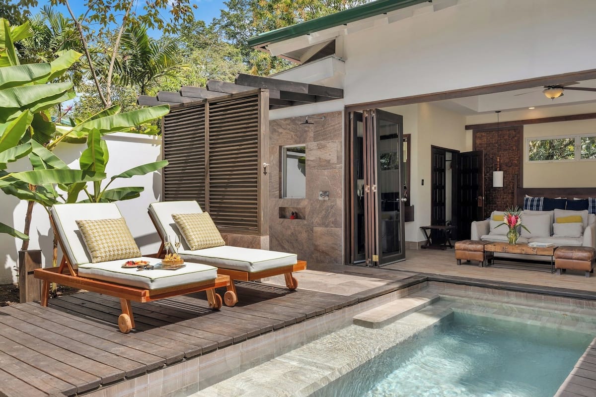 Un área de piscina moderna al aire libre con sillones de descanso, una terraza de madera y vistas a la casa.