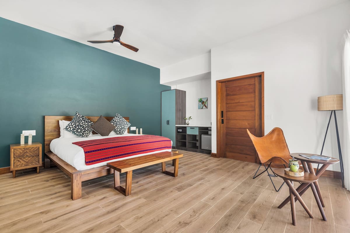 Un dormitorio con cama, banco de madera, silla, escritorio y ventilador de techo.