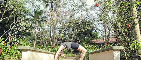 Una persona realizando una postura de yoga sobre un sendero de concreto, rodeada de abundante vegetación y árboles.