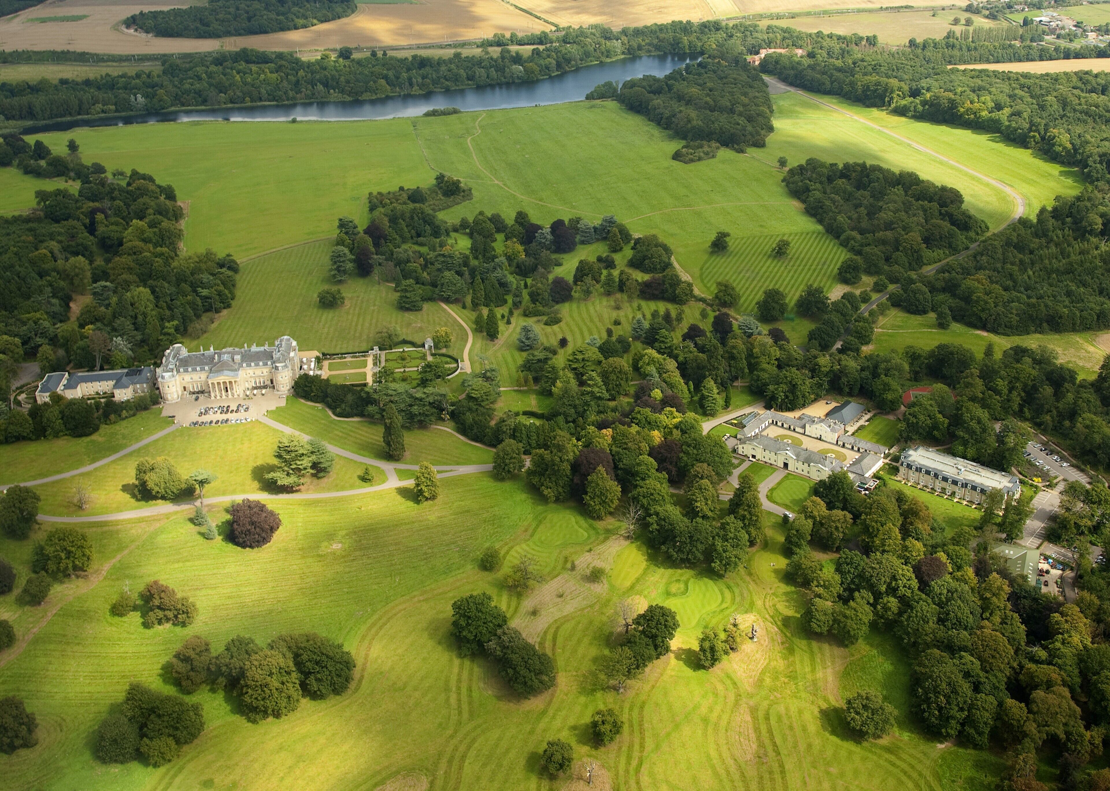 An aerial view of a large estate with a main building, multiple smaller structures, and extensive green fields and forests.