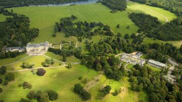 An aerial view of a large estate with a main building, multiple smaller structures, and extensive green fields and forests.
