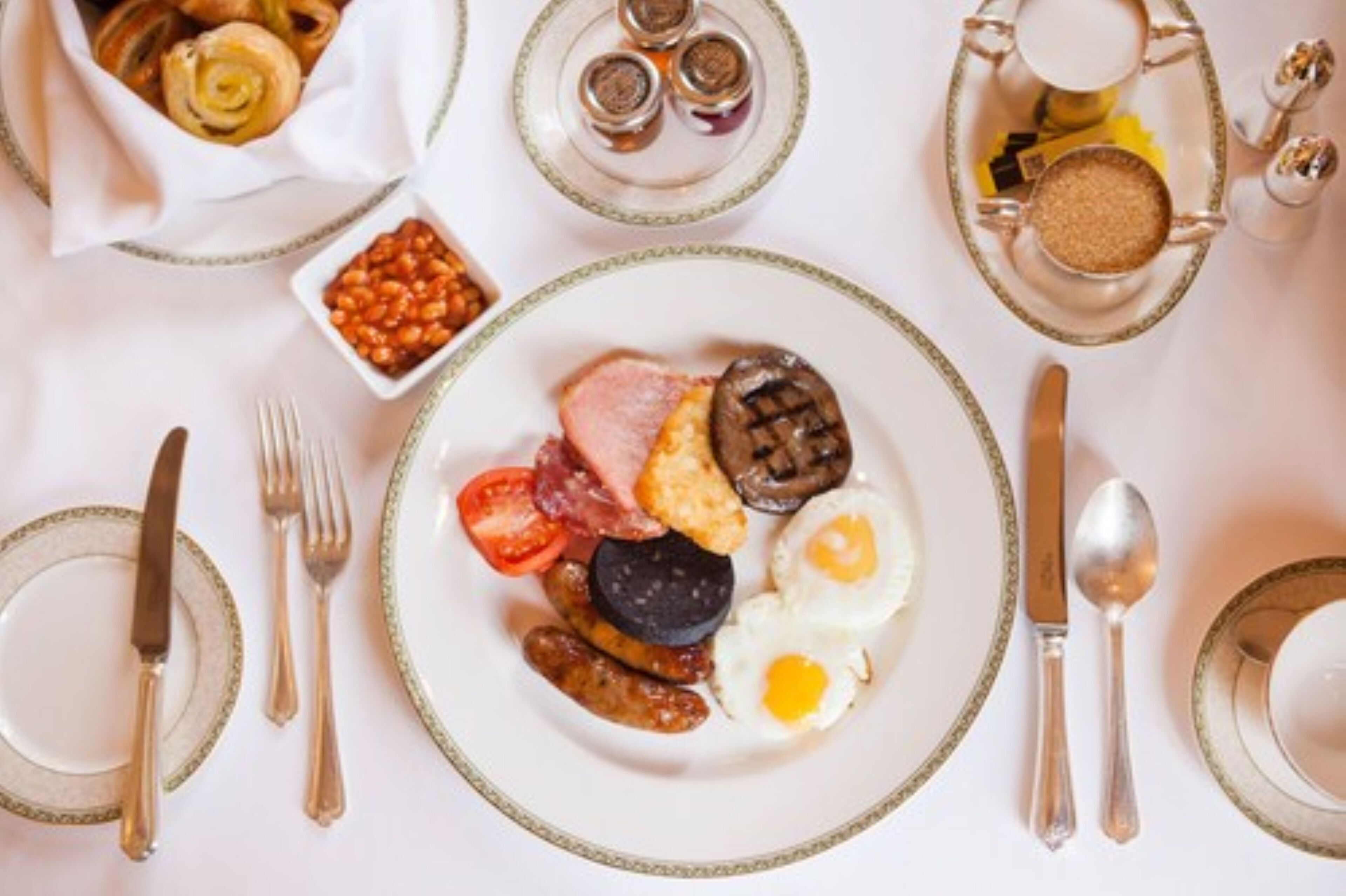 A breakfast setting with a plate of eggs, sausages, tomatoes, and mushrooms.