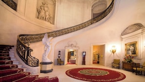 A grand staircase with ornate railings, a red carpeted area, and classical statues. - Luton Hoo Hotel, Golf And Spa (Luton)