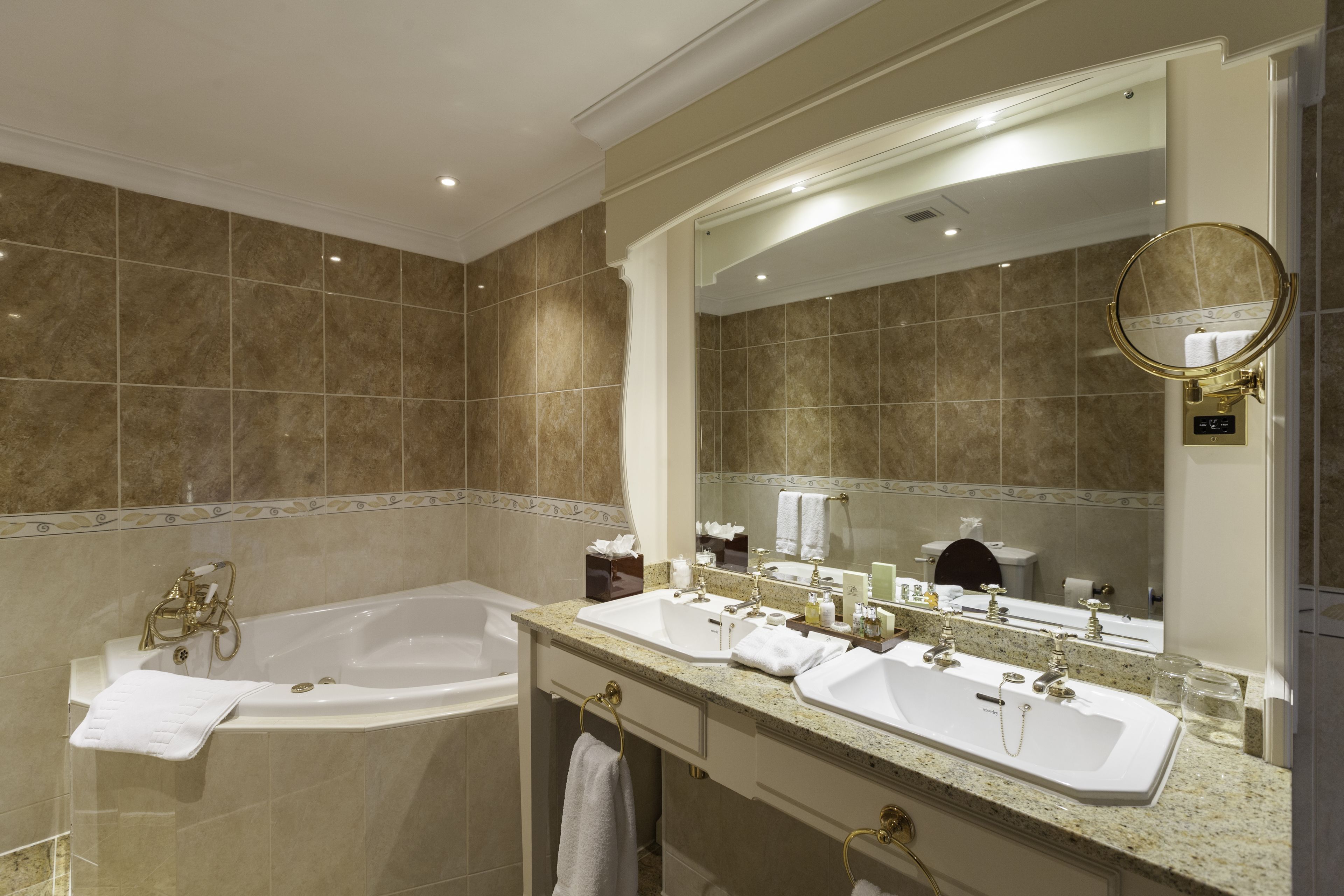 A bathroom with a bathtub, two sinks, a vanity, and a large mirror.