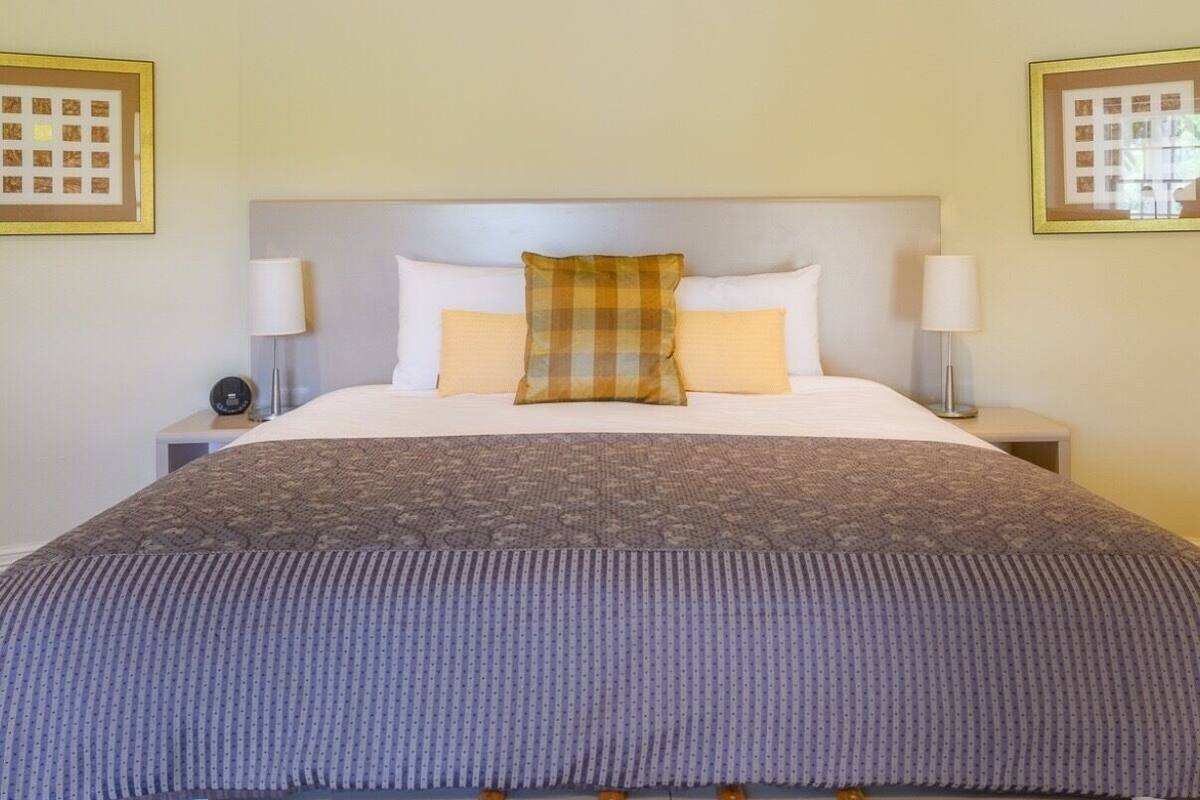 Een hotelkamer met een groot bed, twee nachtkastjes, een hoofdbord en twee aan de muur bevestigde fotolijstjes.
