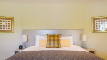 Habitación de hotel con una cama grande, dos mesitas de noche, un cabecero y dos marcos de cuadros en la pared.