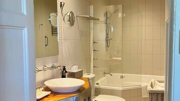 A modern bathroom with a large sink, mirror, toilet, and a glass-enclosed shower area.