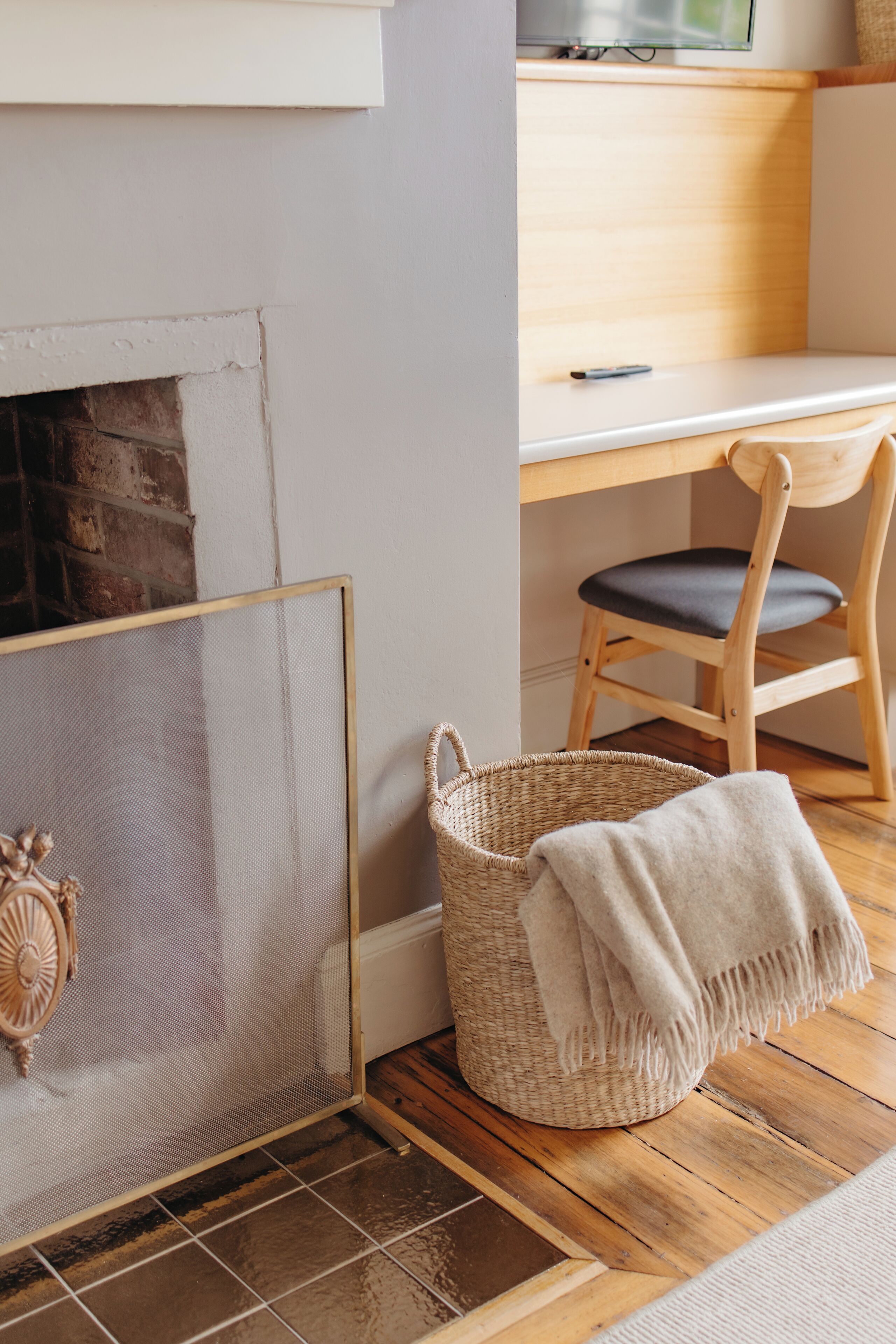 A room with a fireplace, a wooden desk, a chair, and a woven basket.