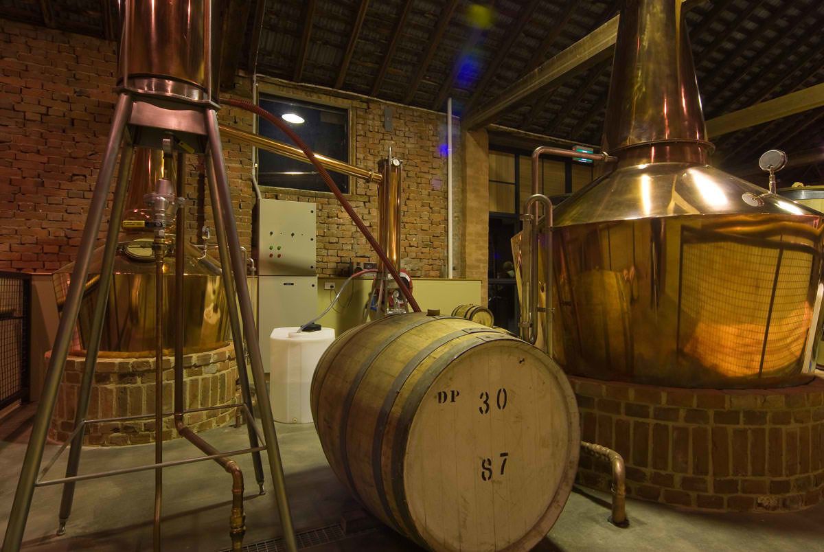 A distillery with copper stills and wooden barrels, indicating a focus on traditional whiskey production.