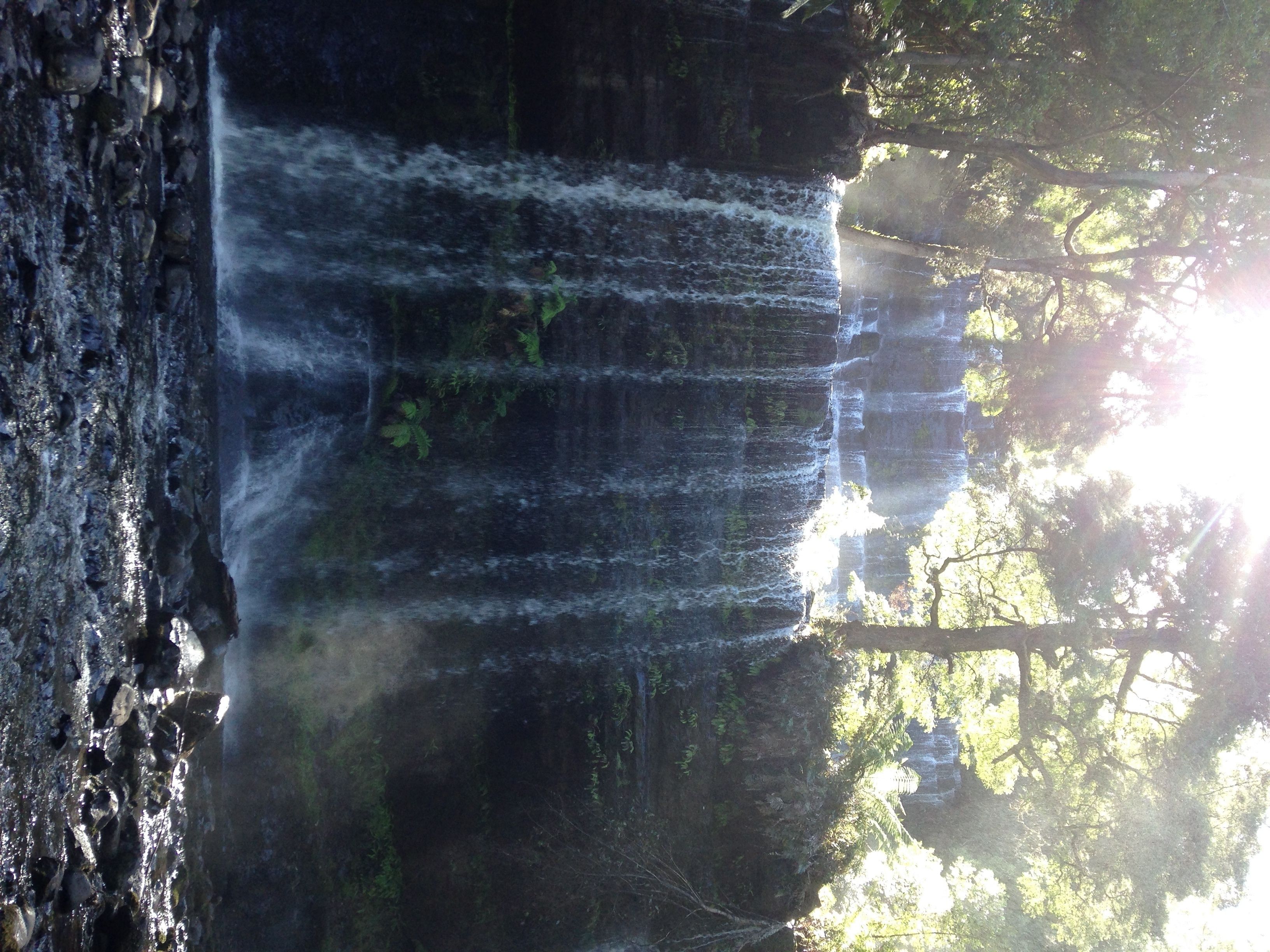 A waterfall cascading over a rocky cliff with sunlight filtering through trees.