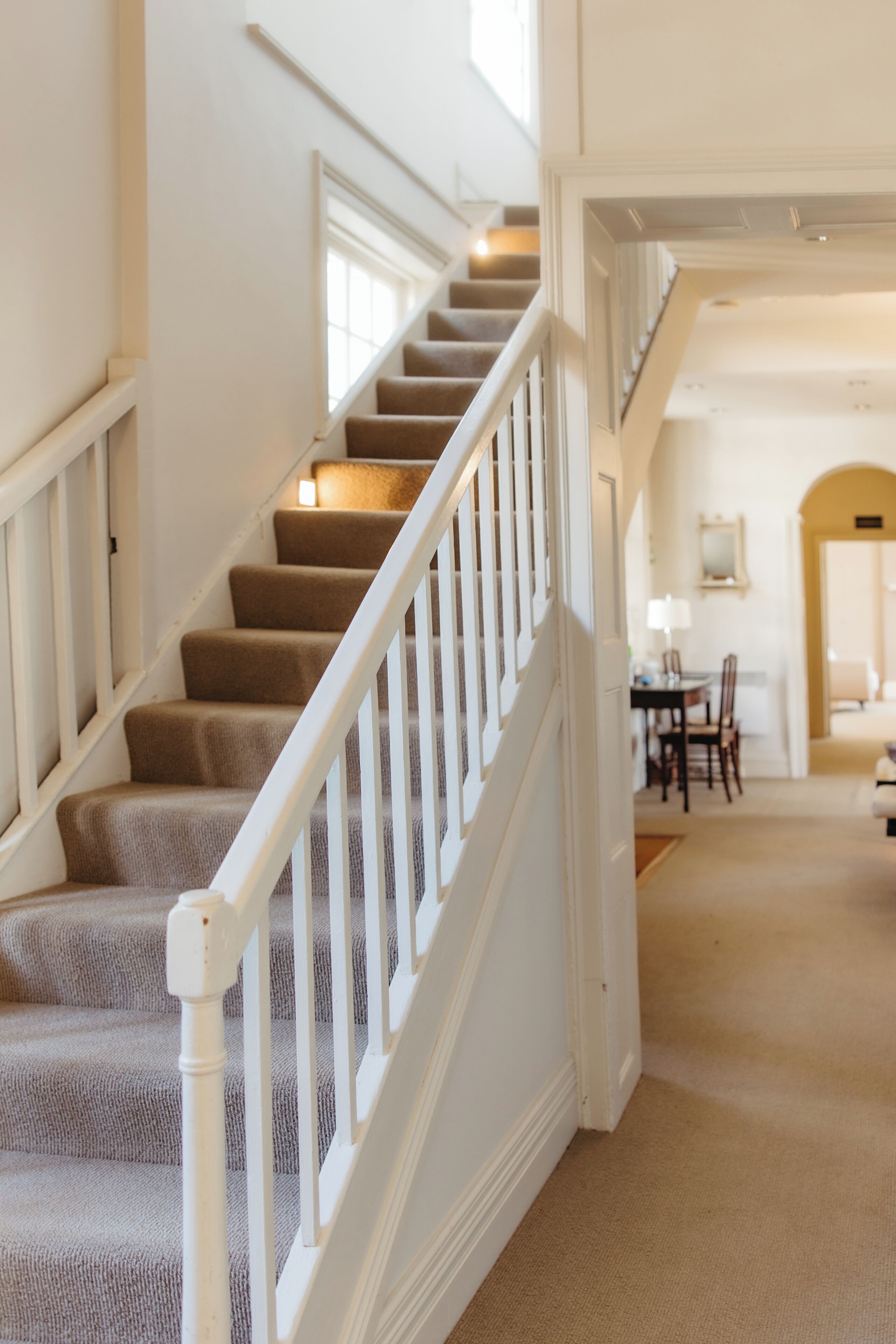 A staircase with white railings and carpeted steps leading to a dining area with a table and chairs.