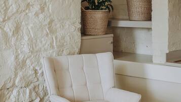 A room with a white upholstered armchair, a wooden floor, a white textured wall, and a wicker basket on a shelf.