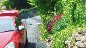 A red car parked on a narrow road with a stone wall on one side and a metal fence on the other.