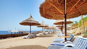 A beach with rows of striped lounge chairs and thatched umbrellas. - Jolie Ville Royal Peninsula Hotel & Resort Sharm El Sheikh (Sharm El Sheikh)