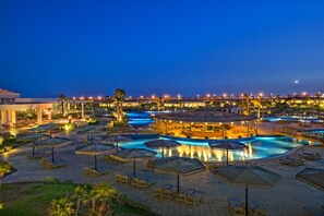 Uma área de piscina em resort, com várias piscinas, espreguiçadeiras e guarda-sóis.
