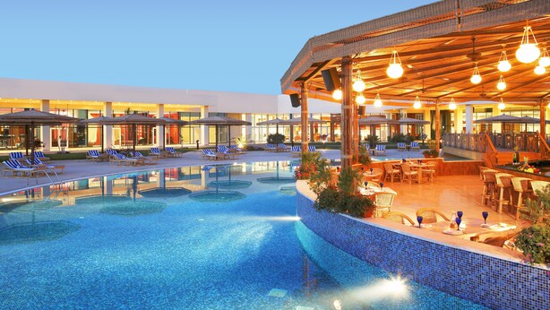A pool area with lounge chairs and umbrellas, a covered seating area with tables, and a building with large windows in the background. - Jolie Ville Royal Peninsula Hotel & Resort Sharm El Sheikh (Sharm El Sheikh)